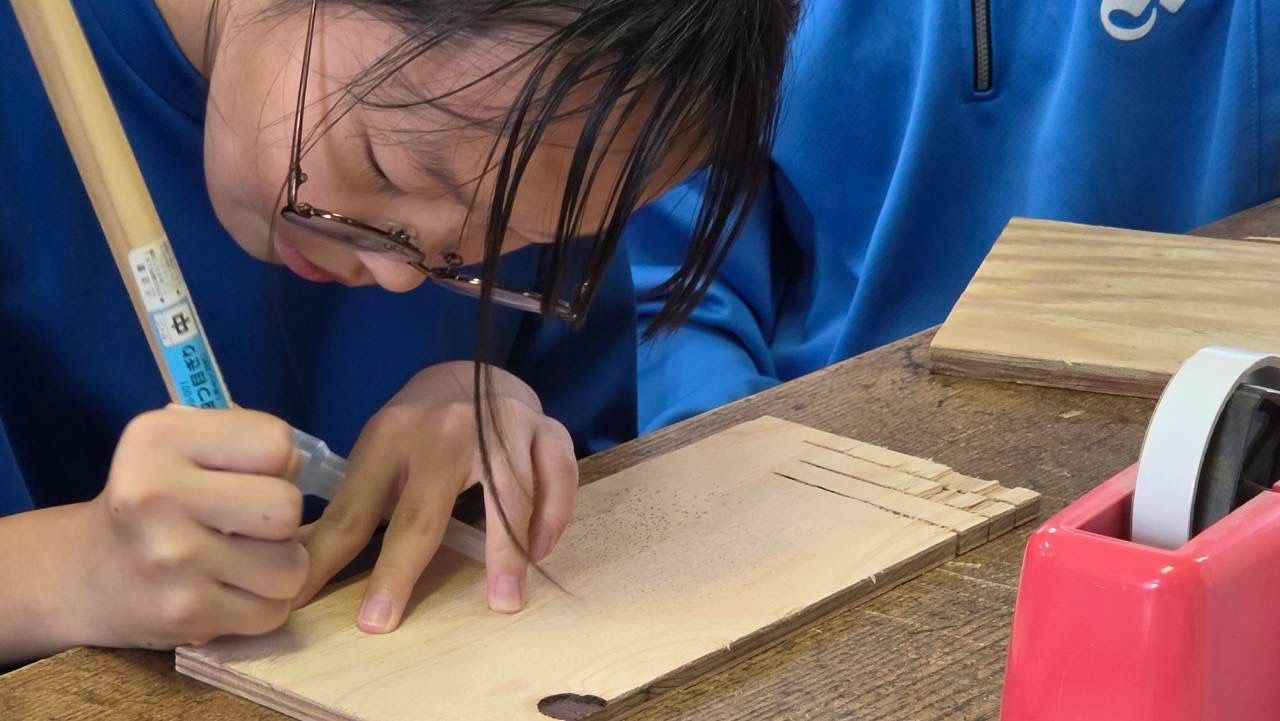 ラベルを貼る板に、筆で線を引く女子
